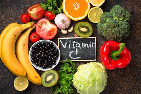 A variety of fresh fruits and vegetables rich in Vitamin C arranged around a small chalkboard with “Vitamin C” written on it.