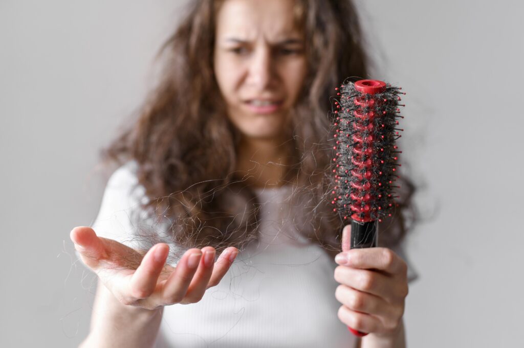 A person holding a hairbrush with strands of hair entangled in it, showing hair loss.